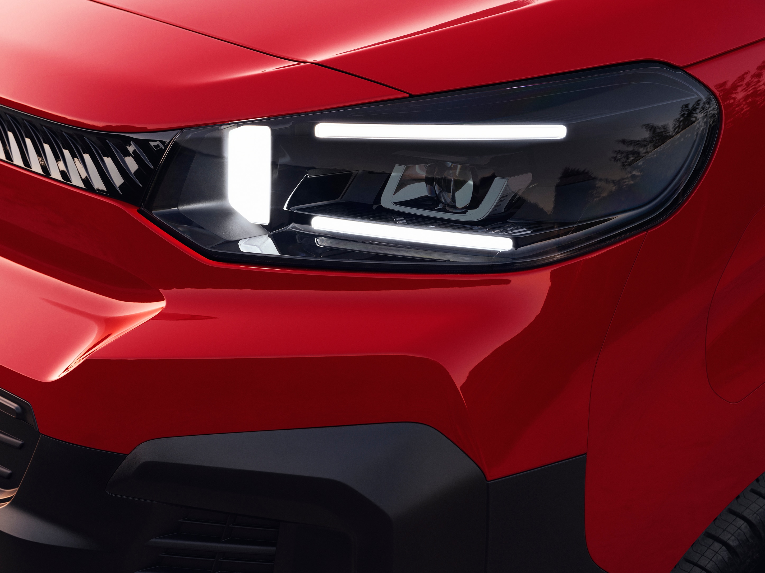 Zbliżenie na przedni reflektor czerwonego Citroëna Jumpy, pokazujące nowoczesny design oświetlenia oraz solidną stylistykę.