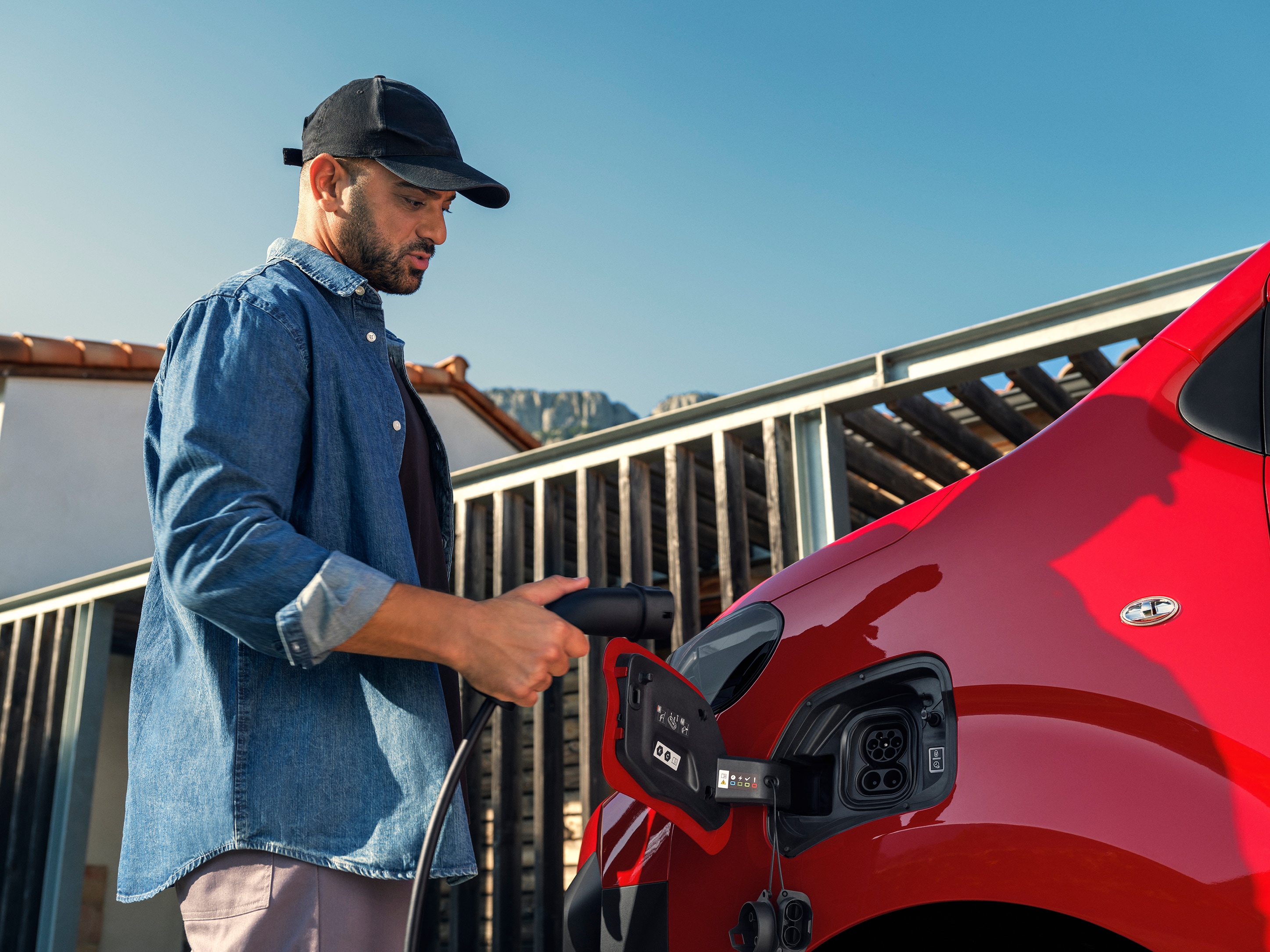 Widok z boku czerwonego Citroëna ë‑Jumpy podłączonego do punktu ładowania, pokazujący łatwość ładowania elektrycznego, korzystanie z rozwiązań łączności oraz praktyczną mobilność w zastosowaniach profesjonalnych.