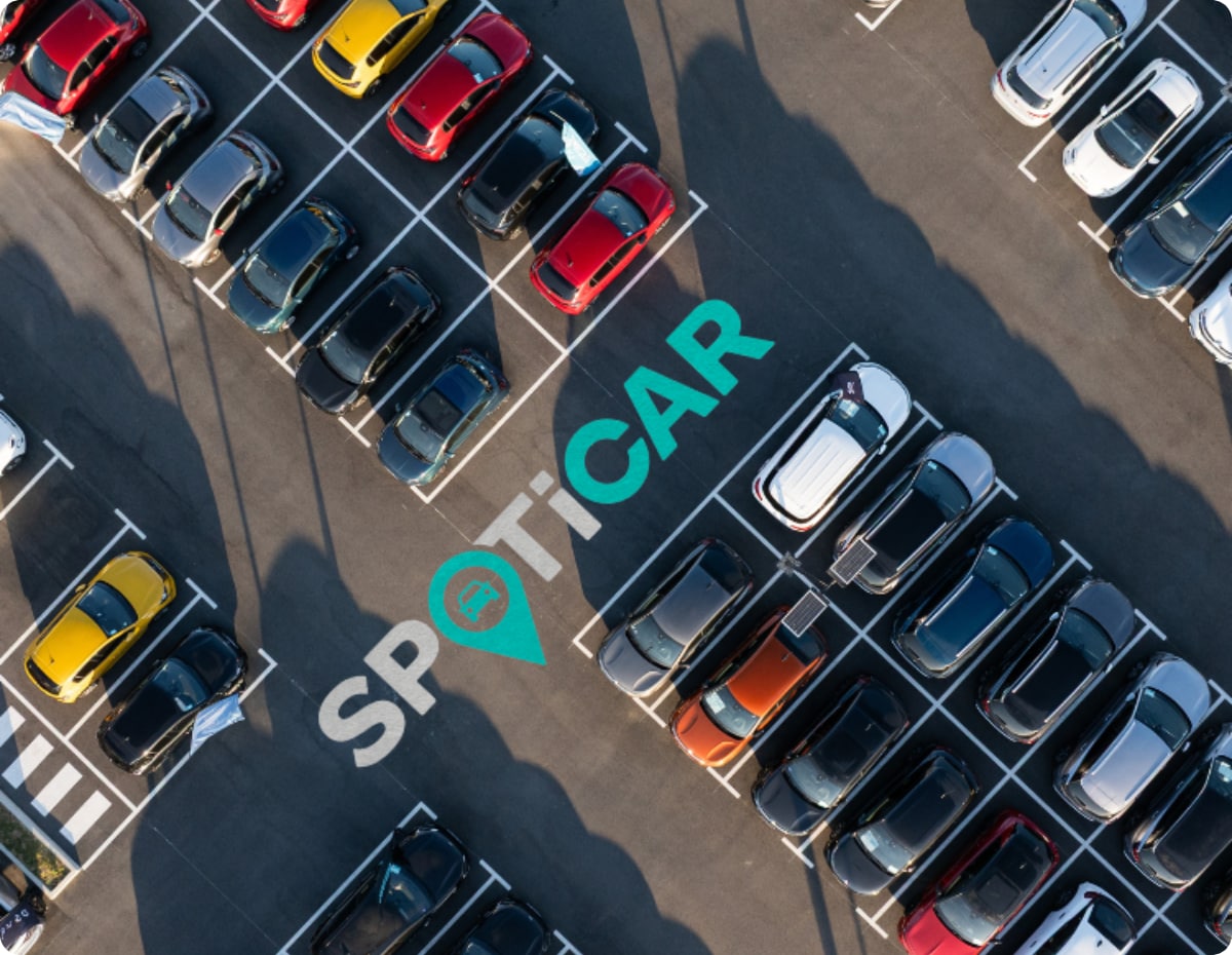 Widok z góry parkingu z wieloma samochodami i oznakowaniem Spoticar, ilustrujący dostępność używanych samochodów marki Citroën.