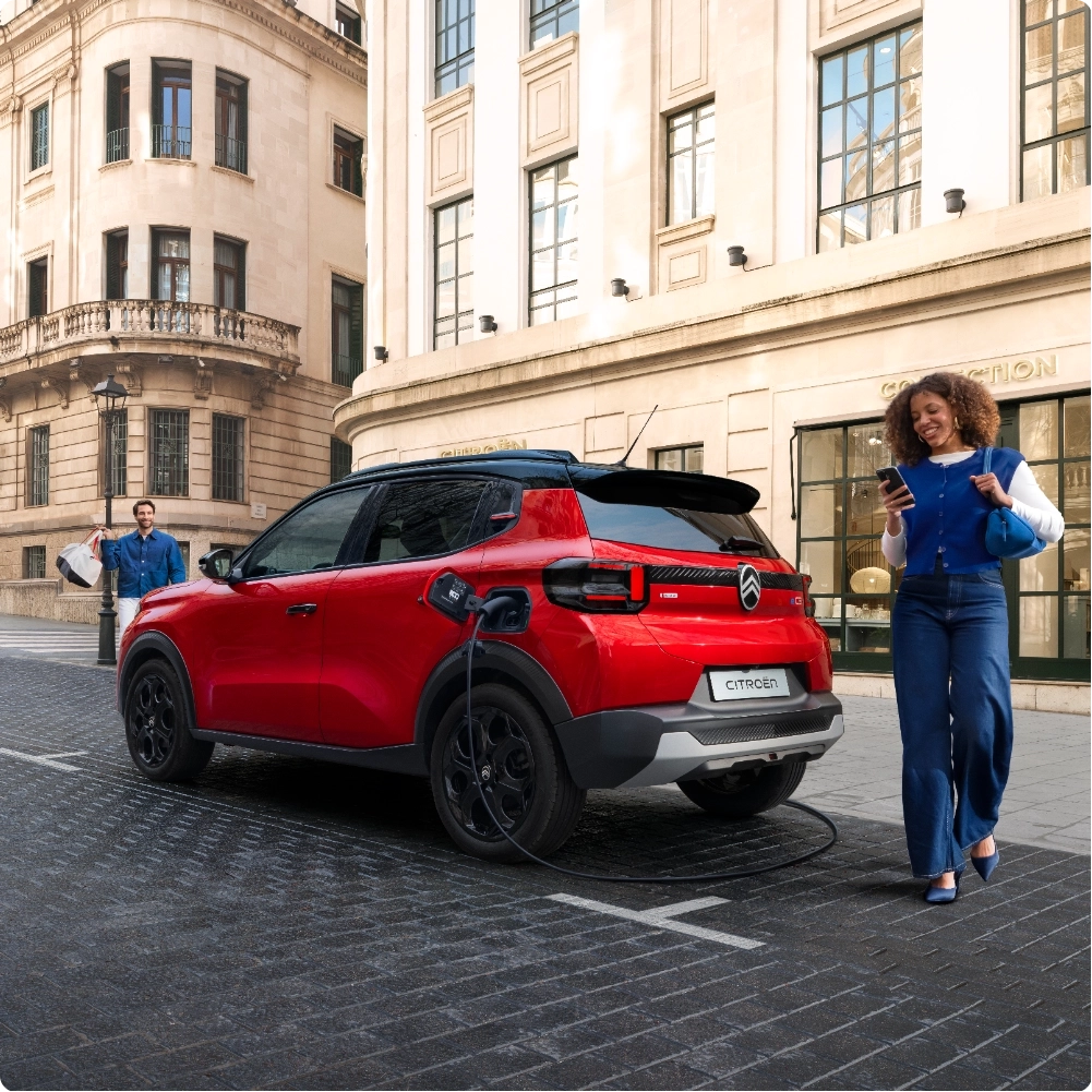 Ujęcie z tyłu w trzech czwartych Citroëna ë-C3 – elektrycznego SUV-a, podczas ładowania na ulicy, podkreślające praktyczny dostęp do bagażnika oraz wygodną, efektywną i przystępną mobilność.