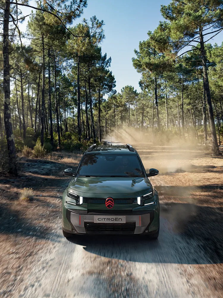 Widok Citroëna ë-C3 Aircross z góry od przodu, ukazujący charakterystyczne światła LED, komfort Advanced Comfort i rodzinnego SUV-a podczas jazdy leśną trasą