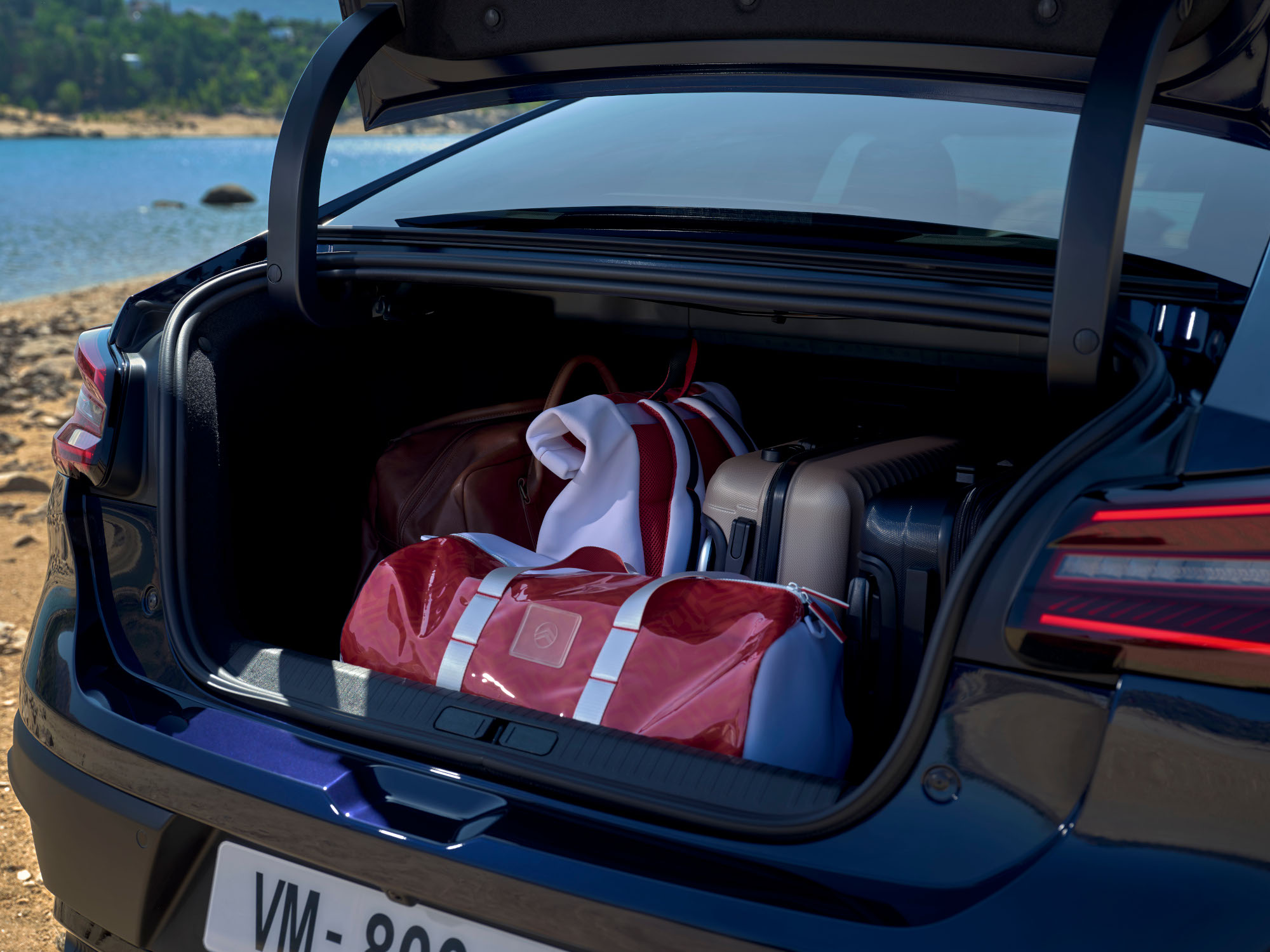 Otwarty bagażnik Citroëna C4 X z walizkami podróżnymi przy jeziorze.