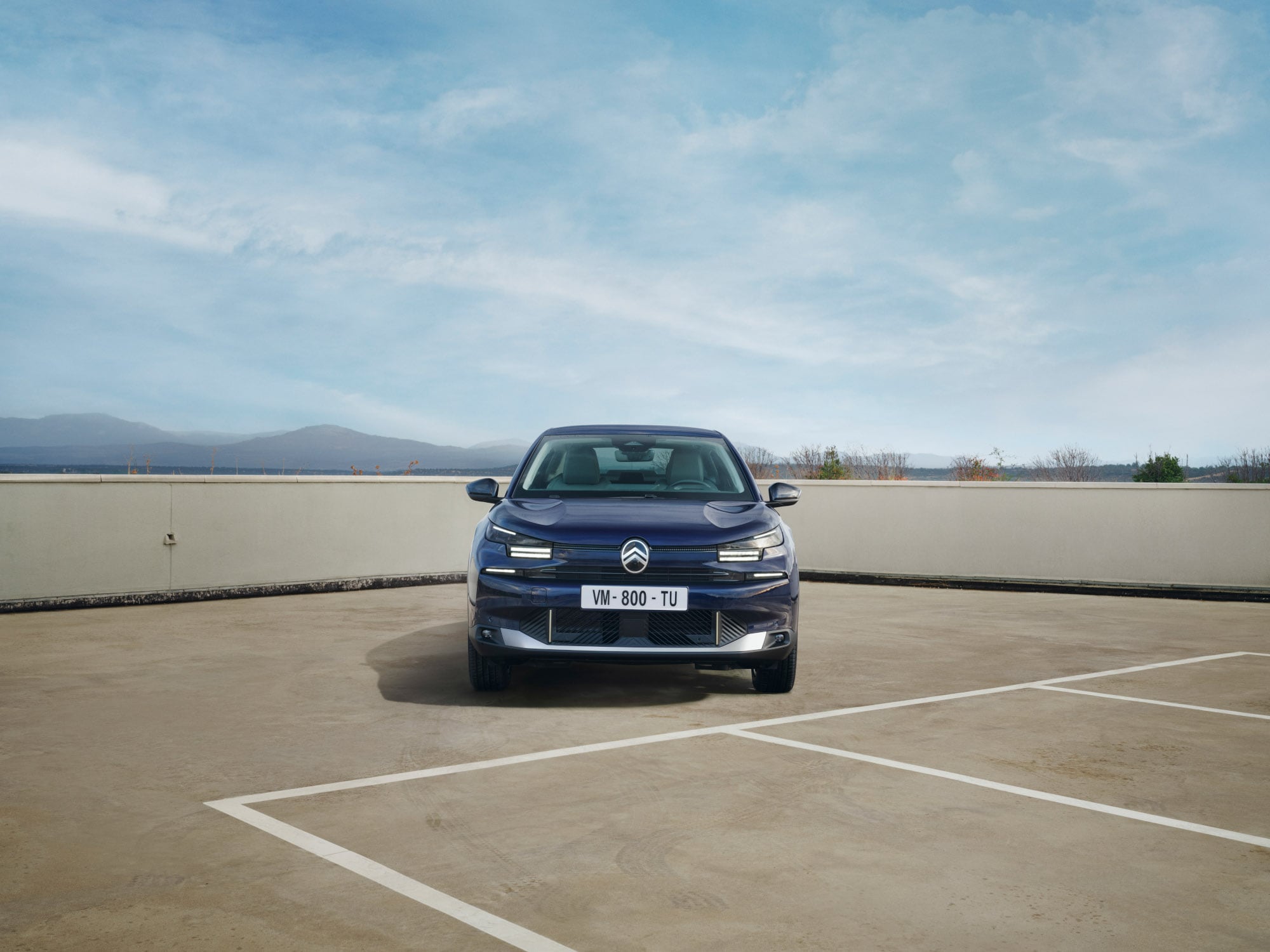 Widok z przodu Citroëna C4 X na parkingu na dachu podkreślający odważną sylwetkę fastback dla pewnej i przystępnej mobilności.