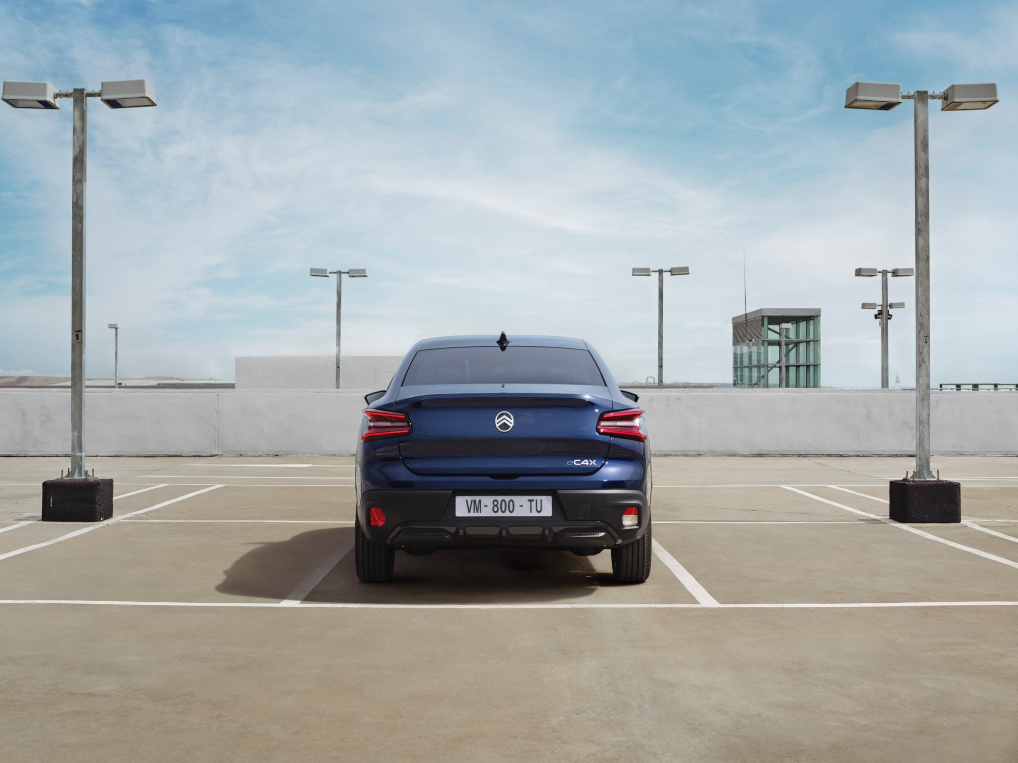 Widok z tyłu Citroëna C4 X na parkingu na dachu prezentujący wyróżniający się design fastback dla stylowej i przystępnej mobilności.