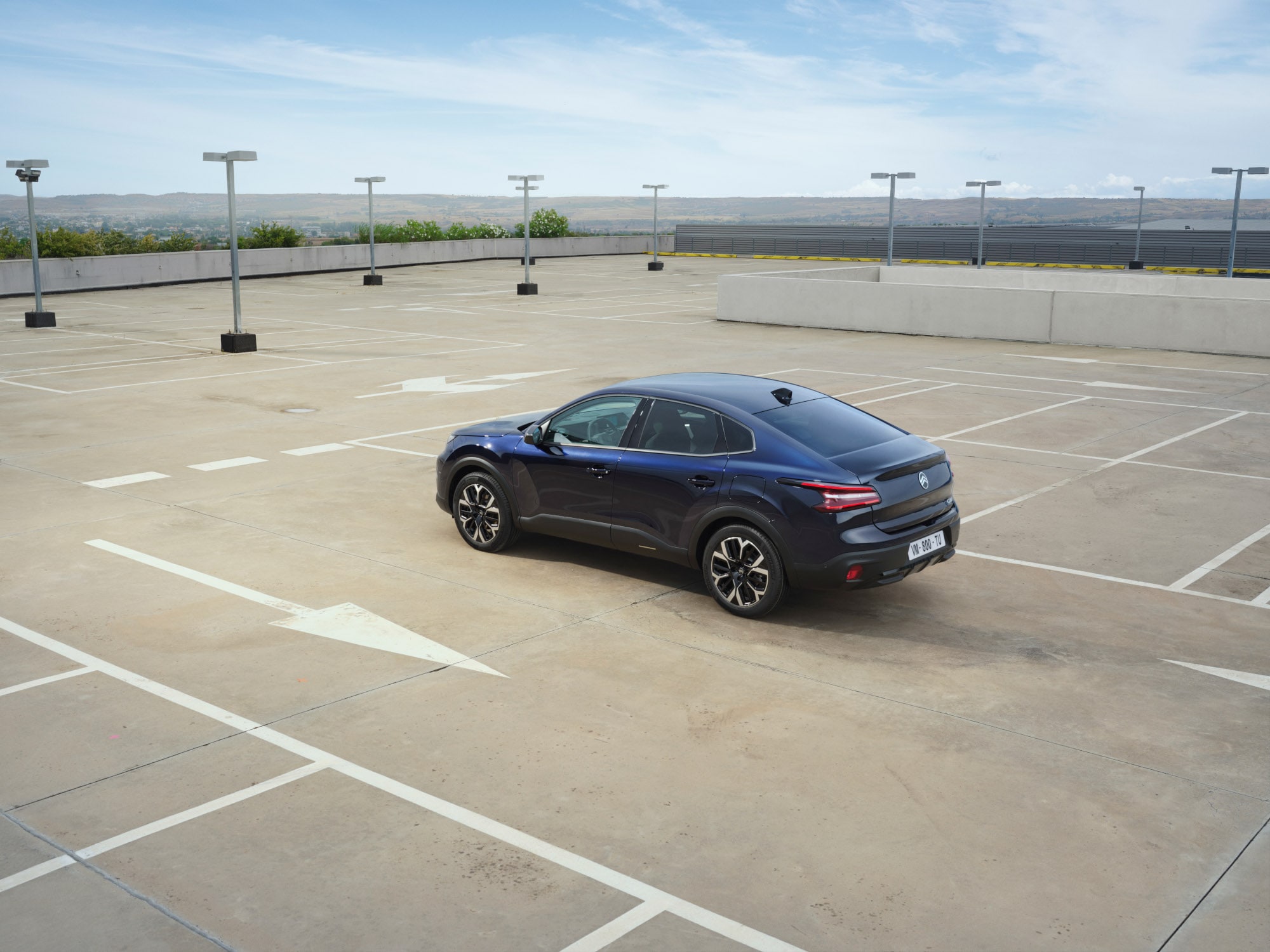 Widok z tyłu pod kątem 3/4 Citroëna C4 X na otwartym parkingu dachowym podkreślający eleganckie linie fastback dla przystępnej mobilności.