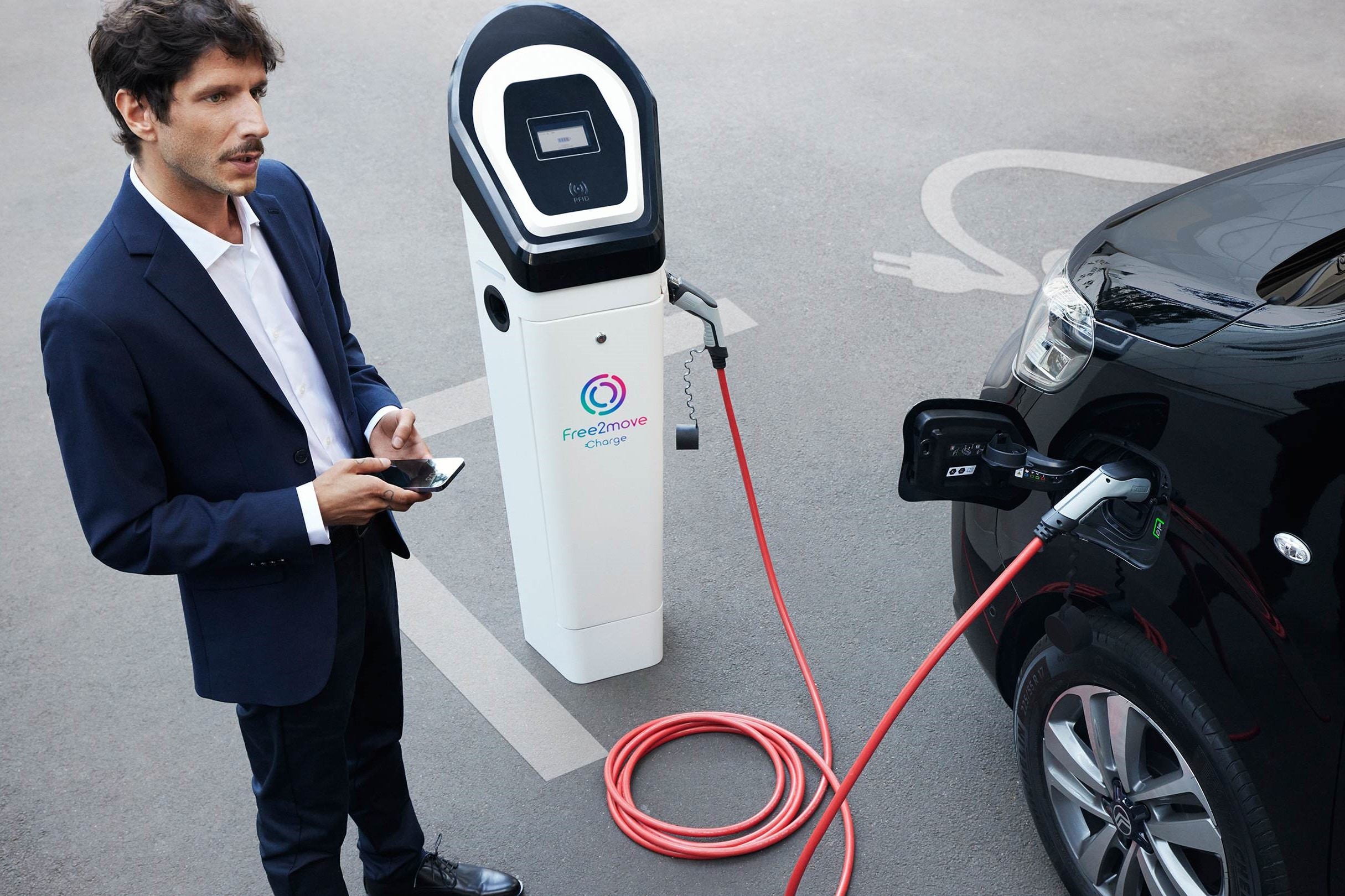 Pojazd elektryczny ładujący się przy publicznej stacji podczas korzystania z aplikacji do zarządzania ładowaniem z Free2move Charge