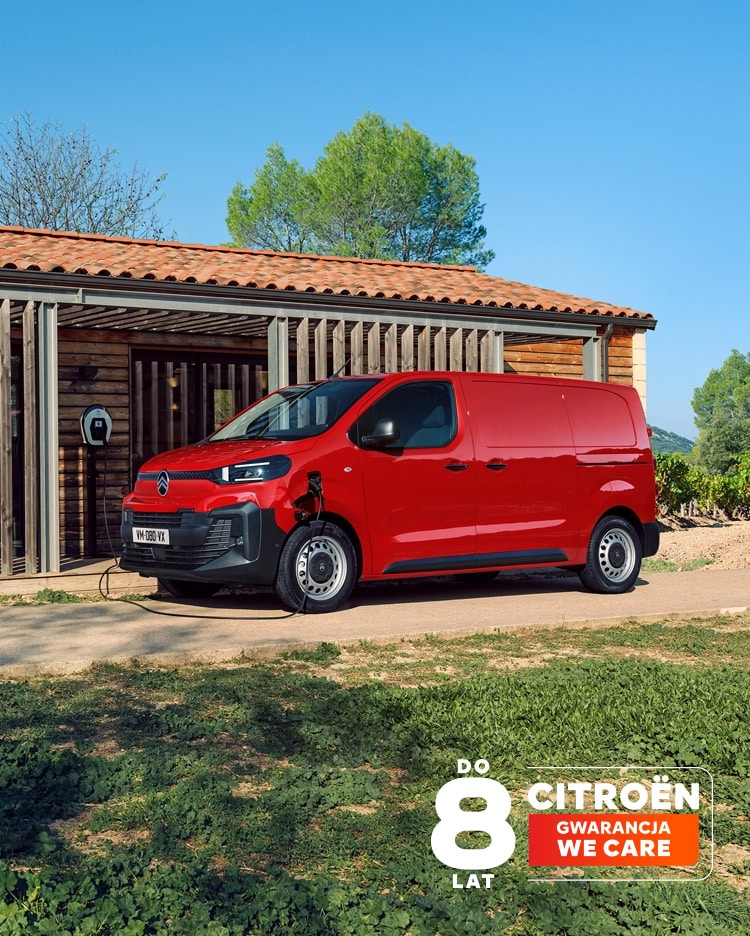 Widok 3/4 z boku czerwonego Citroëna ë‑Jumpy podczas ładowania przed budynkiem, podkreślający nowoczesny elektryczny design, funkcjonalność, łączność i pewną, profesjonalną prezencję.